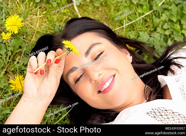 Happy woman with yellow flower lying on grass