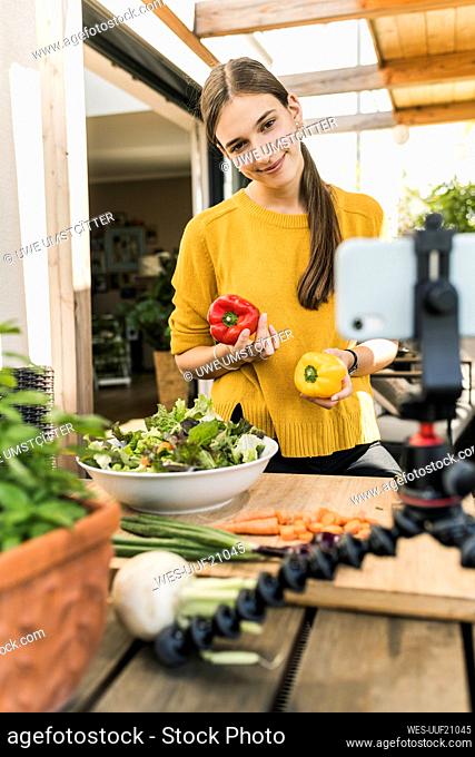 Smiling woman filming with mobile phone while preparing food at home