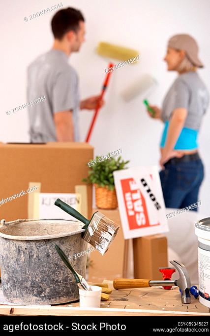 Young couple painting their new house with paint roller, equipment in focus