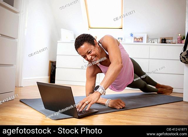 Happy mature woman exercising at laptop on yoga mat
