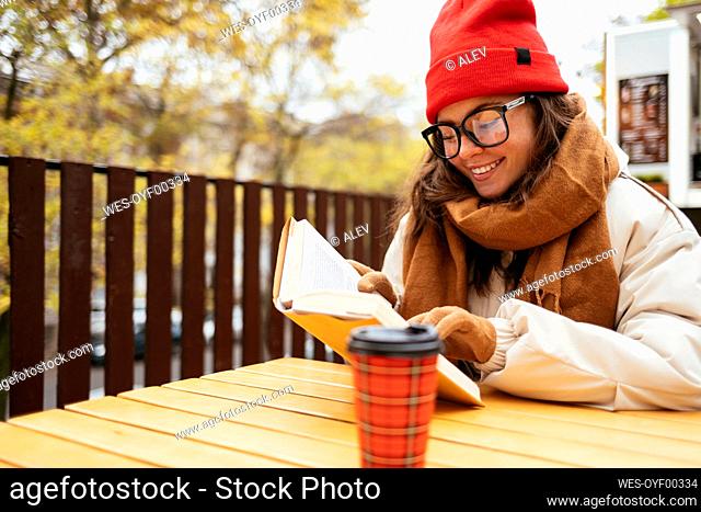 Woman smiling while reading book sitting at sidewalk cafe
