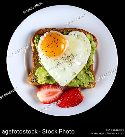 Toast with avocado and egg with heart shape on white plate isolated on black background