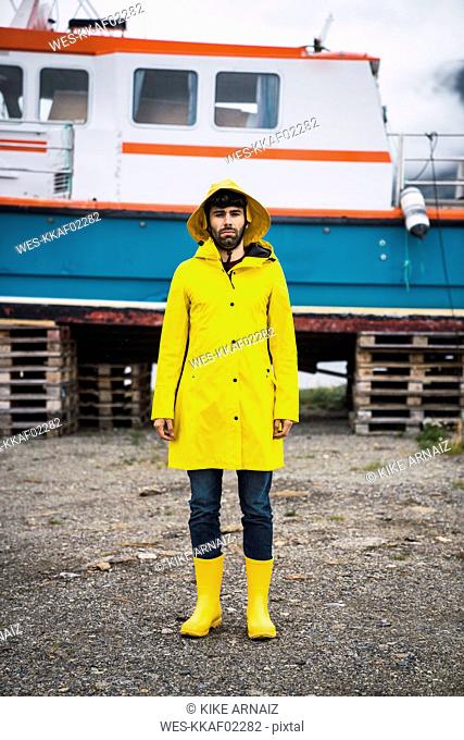 Young man standing in front of a ship, wearing rain clothes, Lapland, Norway
