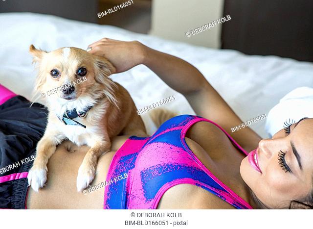 Hispanic athlete petting dog on bed