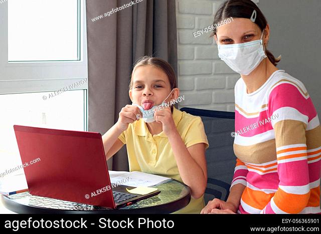 The girl took off her medical mask and showed her tongue, doing homework in self-isolation mode