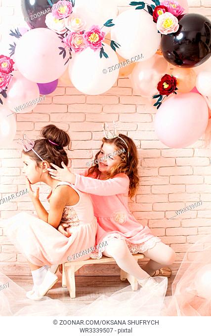 Two beautiful little girls with crowns under birthday balloon and paper flower arch decorations. Childish photozone for celebration