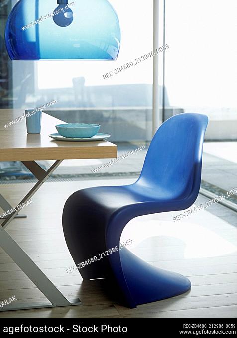 Blue moulded plastic chair at table with blue glass hanging lamp