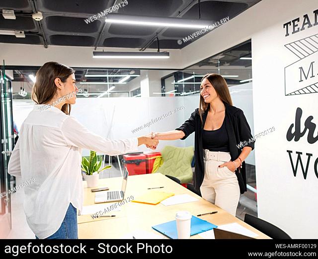 Happy businesswomen shaking hands in conference room at office