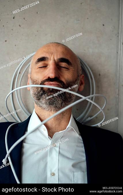 Mature businessman with computer cable leaning on wall