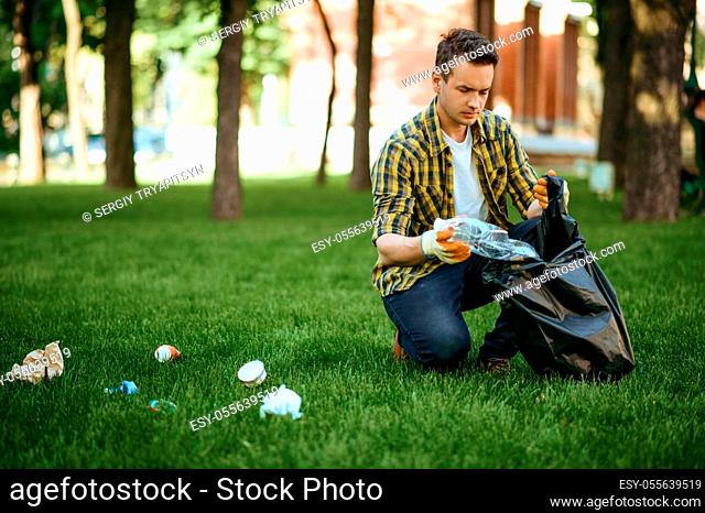 Young man collects garbage in a bag in park, volunteering. Male person cleans forest, ecological restoration, eco lifestyle, trash collection and recycling
