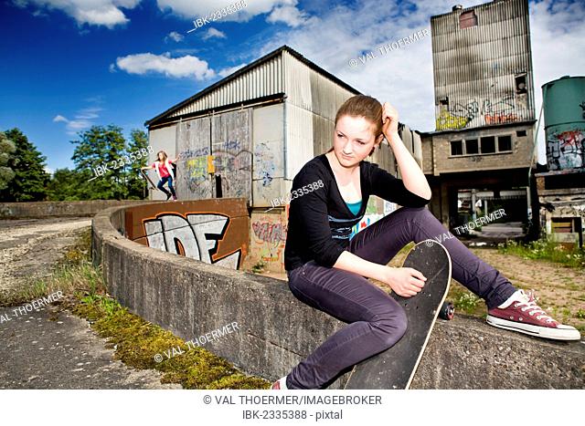 Portrait of a young teenage girl with a skateboard sitting in an urban area