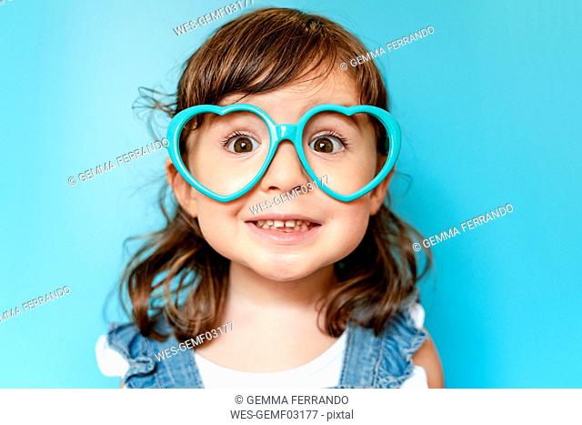 Portrait of cute little girl with heart shaped glasses on blue background