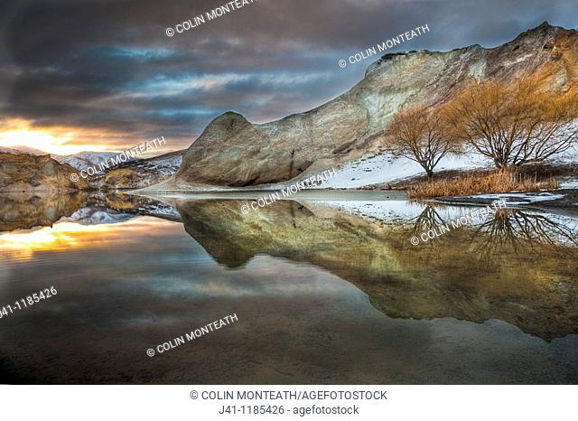Blue Lake reflections of clay cliffs at sunset, after winter storm and snowfall, St Bathans, Central Otago, New Zealand