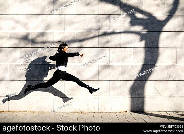 Young woman making a big jump on a wall with a shadow of a tree