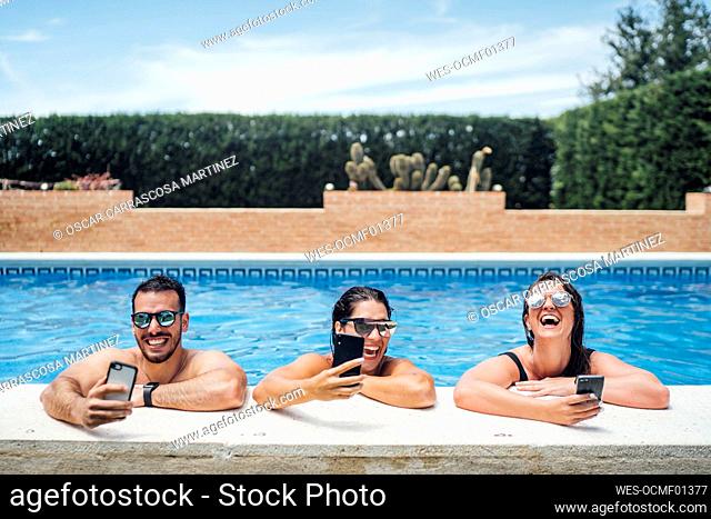 Laughing friends during pool party using smartphones