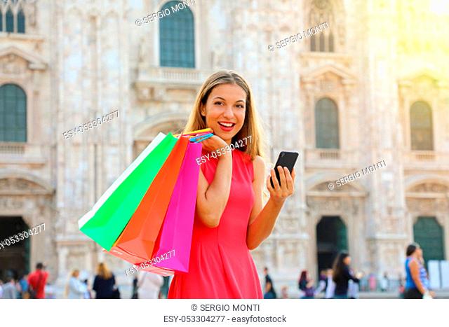 Shopper woman looking at the camera doing shopping with a smartphone in a commercial square