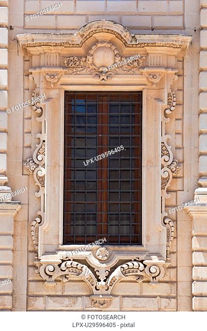 Window detail: ornate Baroque facade of Palazzo del Seminario, ornately carved in Leccese style, grid of metal bars across window, Lecce, Salento, Puglia