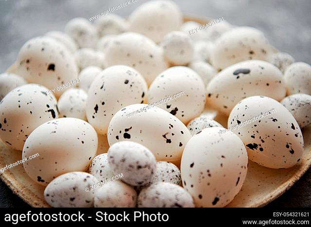 Composition of white traditional dotted Easter eggs in white ceramic plate placed on gray stone background. High angle shot