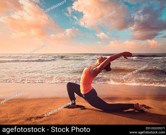 Vintage retro effect filtered hipster style image of Yoga outdoors - sporty fit woman practices yoga Anjaneyasana - low crescent lunge pose outdoors at beach on...