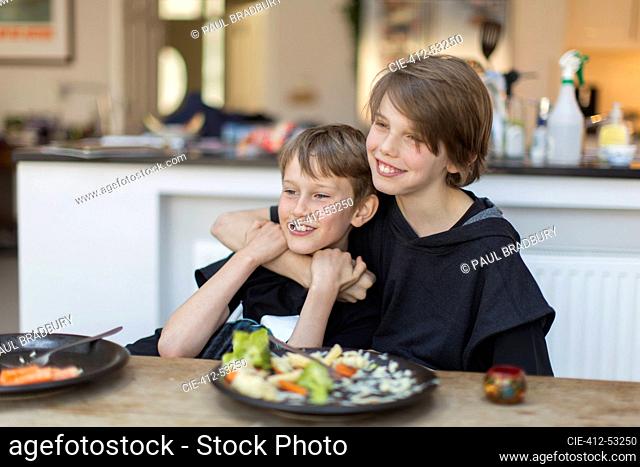 Happy brothers hugging and eating dinner at dining table