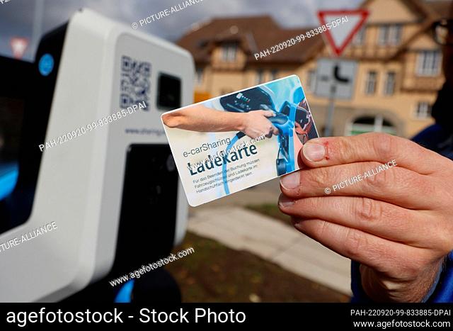 20 September 2022, Saxony-Anhalt, Wernigerode: Lars Bollmann from the Wernigerode municipal utility holds a charging card to an electric car