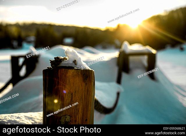 Snow covered jetty wood poles in front of a blurry sunset background with lens flares