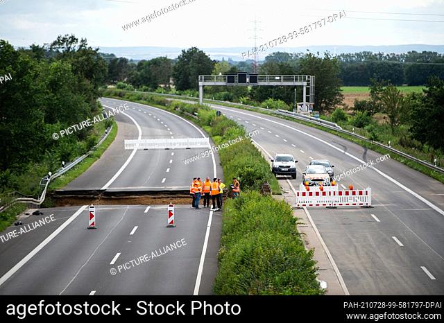 28 July 2021, North Rhine-Westphalia, Erftstadt-Blessem: Workers stand on the A1 motorway inspecting a collapsed section of road
