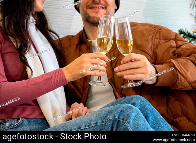 Romantic smiling lovers sitting on sofa and clinking glasses of champagne in living room. Christmas, New Year and love concept