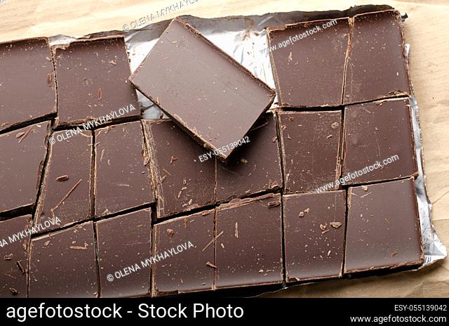 Dark chocolate bar broken into pieces laying in a foil on paper wrap