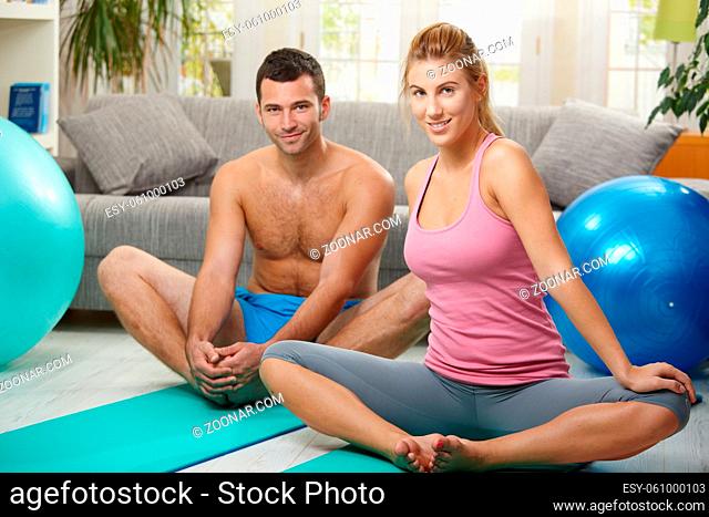 Young couple sitting on fitness mattress and streching before exercises