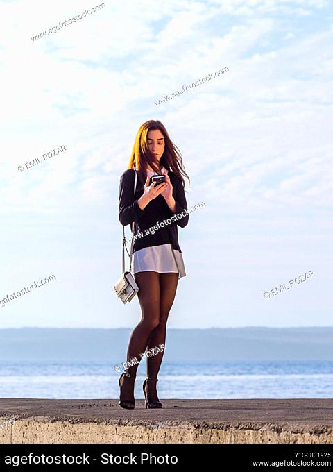 Teenage girl walking on seaside using her smartphone for talking
