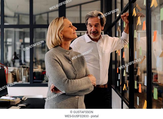 Businessman and businesswoman working on sticky notes at glass pane in office