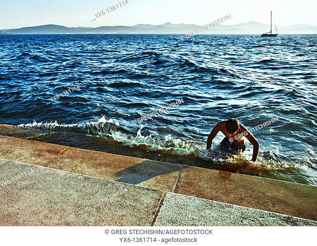 A swimmer getting out of the water at the steps of the Sea Organ in Zadar, Croatia  Designed by architect Nikola Basic, 35 organ pipes are built under the steps...