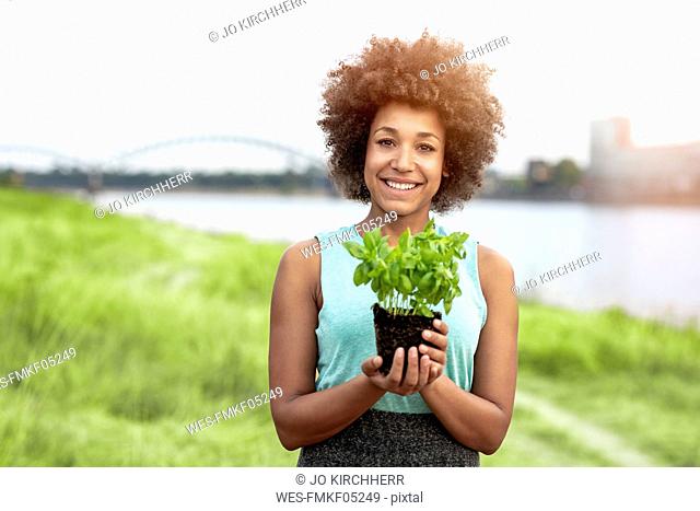 Portrait of smiling woman holding plant outdoors