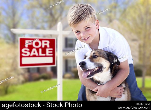 Happy young boy and his dog in front of for sale real estate sign and house