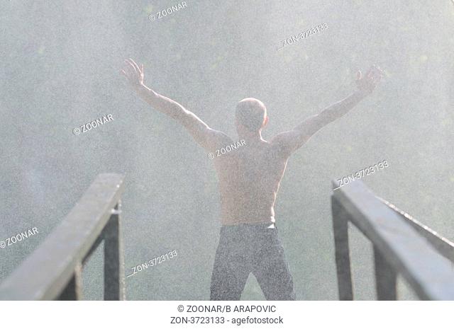 standing man with wide opened arms with waterfalls in background and representing freshness healthy lifestyle and success concept