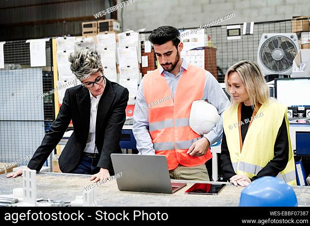 Engineer with colleagues discussing over laptop in industry