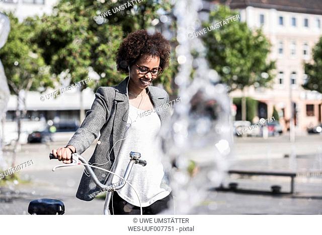 Portrait of smiling woman with bicycle listening music with earphones