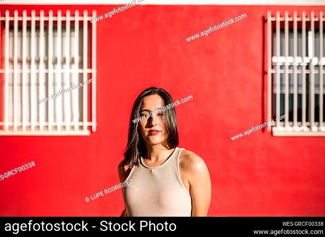 Portrait of beautiful brunette young woman at a red house wall outdoors