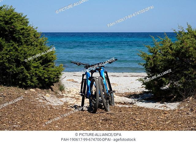 05 June 2019, Italy, Nuoro: Two bicycles are set on the beach in the National Park di Bidderosa in the Gulf of Orosei. Photo: Jens Kalaene/dpa-Zentralbild/ZB