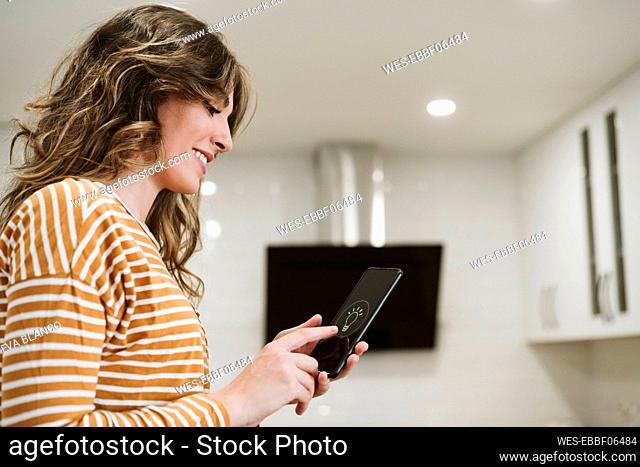 Young woman using mobile phone with smart home app for lighting at home