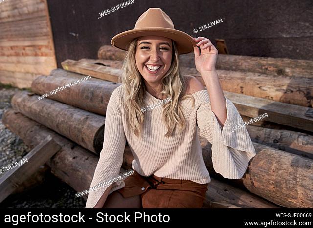 Cheerful beautiful woman wearing hat sitting on logs