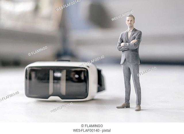 Miniature businessman figurine standing next to VR glasses
