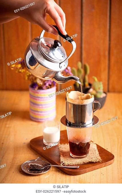 Woman left hand pouring hot water into Vietnamese style coffee dripper above vintage glass to make Thai tea in cafe