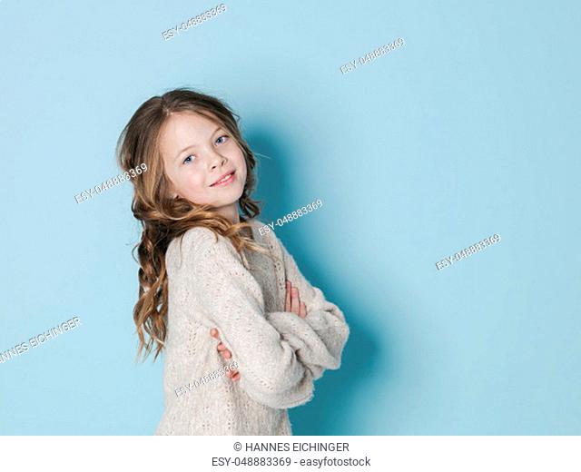 pretty and cool 9 year old girl with brown wool sweater posing in front of blue background in the studio