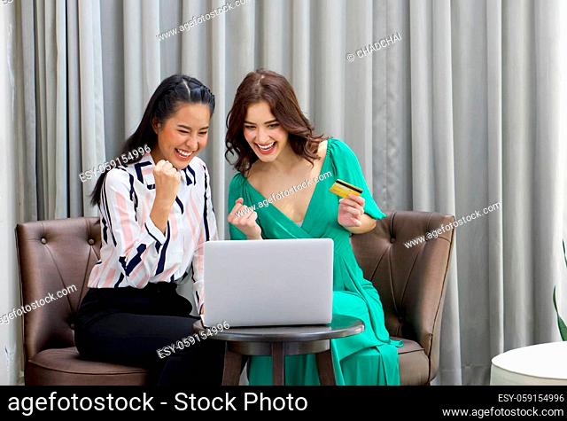 Young woman in green clothes and her friend spend time together on holidays in the living room. Both raised their fist up and smiled happily after shopping good...