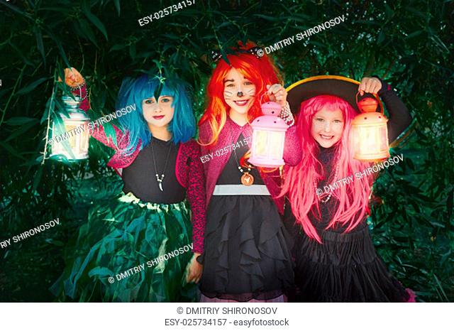 Little girls in wigs and Halloween costumes holding lanterns and looking at camera