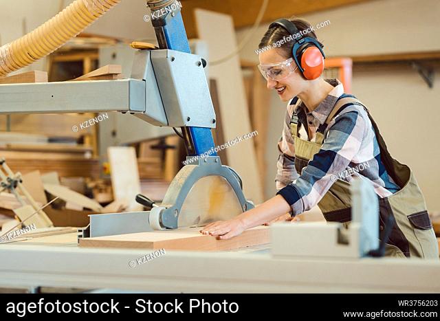 Woman carpenter working with wood at the table saw in her workshop