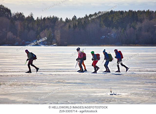 Long distance ice skaters on Lake Malaren and in foreground unmanned ice fishing hole, Sigtuna, Sweden, Scandinavia