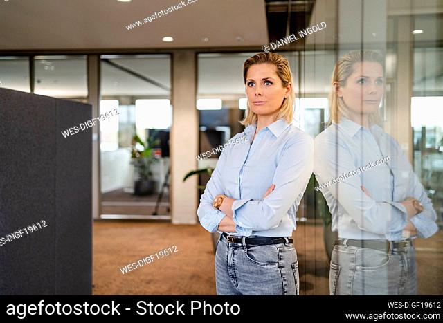 Contemplative businesswoman with arms crossed standing near glass wall